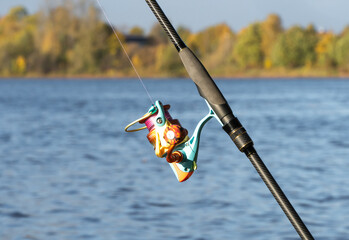 Carbon spinning rod, lying on the background of a river or lake with a colored reel and silicone baits. Catching walleye on a jig head and a pull-off leash. Fishing on the banks of a river or lake. 