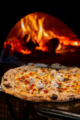 Pizza topped with creamy ricotta coming out of a wood fired oven