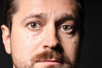 Sad man crying on black background, closeup