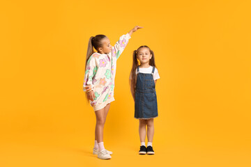 Naklejka premium Little girls comparing their heights on orange background