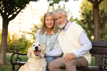 Portrait of happy senior couple with adorable Golden Retriever dog on bench outdoors