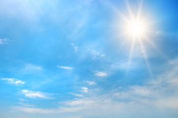 Bright blue sky with shining sun in upper corner and scattered white clouds illuminated by sun rays creating glowing daytime atmosphere with copy space