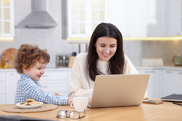 Smiling woman typing on laptop with her son at wooden desk in home office