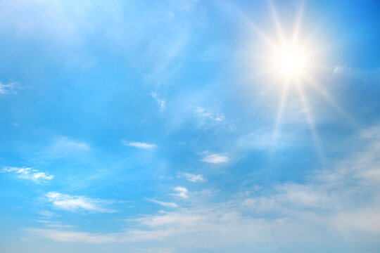 Bright blue sky with shining sun in upper corner and scattered white clouds illuminated by sun rays creating glowing daytime atmosphere with copy space