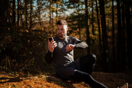 Male runner checking time and using smartphone app in forest