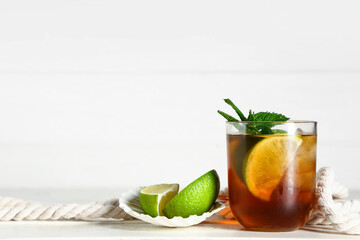 Glass of cold Cuba Libre cocktail with rope on white wooden background