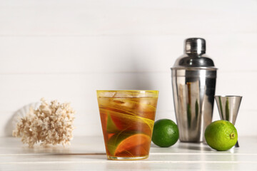 Glass of cold Cuba Libre cocktail with coral, shaker and measure cup on white wooden background