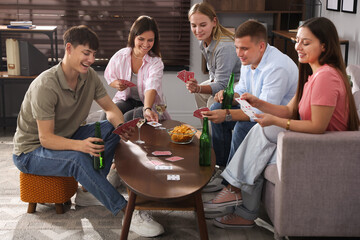 Group of friends playing cards at wooden table indoors