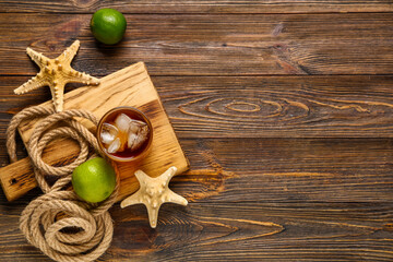 Board with glass of cold Cuba Libre cocktail, starfishes and rope on wooden background