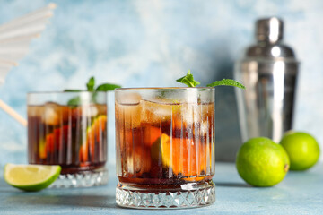 Glasses of cold Cuba Libre cocktail with shaker on blue grunge background