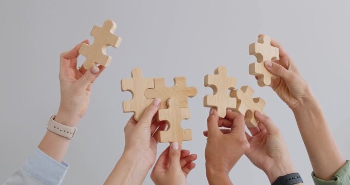 Hands hold puzzle pieces for team solution. Raised hands join wooden pieces, showing teamwork, collaboration, planning and strategy to connect ideas. Teamwork and connection guide concept.