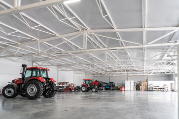 Modern agricultural warehouse with red tractors and farming equipment storage space. © DedMityay