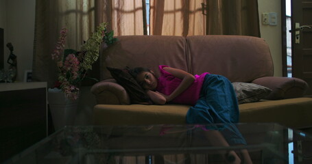 Young girl lying on a couch indoors, embodying solitude and emotional distance, reflecting themes...