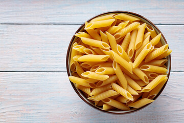 Dry Yellow Penne Pasta in Bowl on Wooden Background Top View Copy Space
