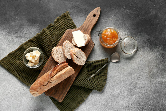 Sliced bread with butter and jar of apricot jam on grey grunge background