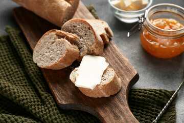 Sliced bread with butter and jar of apricot jam on grey grunge background