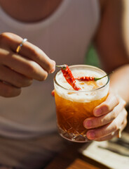 A bartender pouring a vibrant margarita into a chilled coupe glass, orange peel twist and salt rim visible, moody bar lighting with elegant presentation and negative space.