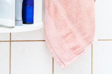 Soft pink terry cloth towel hanging near bathroom shelf with hygiene products