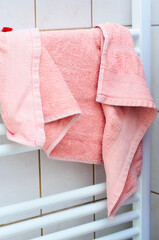 Soft pink terry cloth towel drying on a white heated bathroom rack