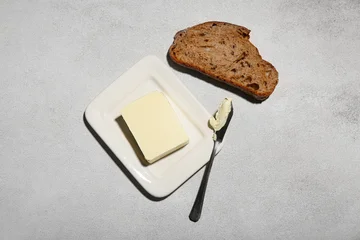 Fototapete Zu Essen Slice of fresh bread, dish with butter and knife on grey grunge background  © Pixel-Shot