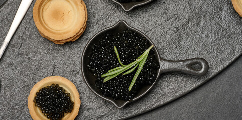 Black caviar in cast iron pans and tartlet on dark board.