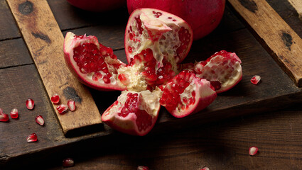 A fresh pomegranate slice with brightly colored seeds on a brown wooden board. Still life against a...