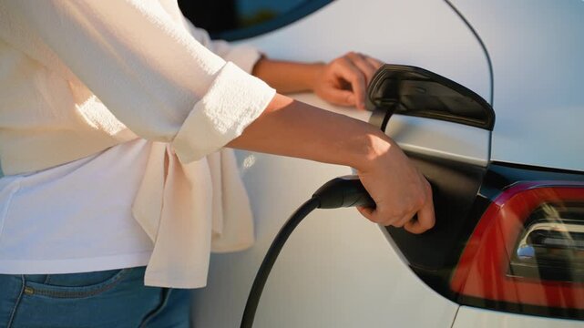 Woman disconnecting power cable from electric car
