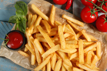 Tasty french fries with basil leaves, tomatoes and bowl of ketchup on wooden background