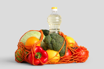 Mesh bag with vegetables, fruits and bottle of oil on grey background