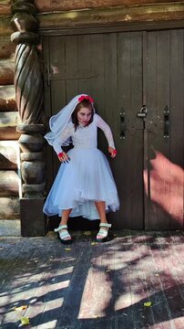 A girl in a white dress and a veil, the image of a scary bride, moves like a zombie on the street, in the park on Halloween