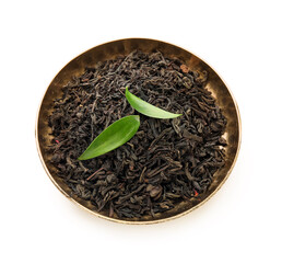 Plate with dry black tea and leaves on white background