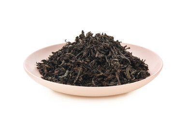 Plate with dry black tea leaves on white background