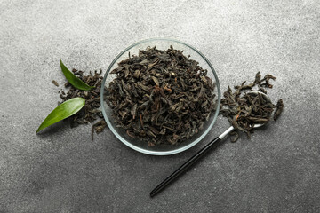 Fototapeta premium Bowl of dry black tea leaves with spoon on white background