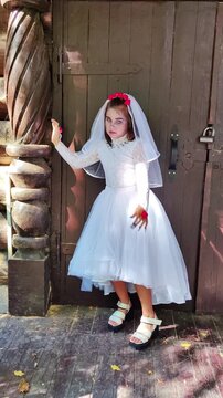 A girl in a white dress and a veil, the image of a scary bride, moves like a zombie on the street, in the park on Halloween