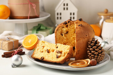 Plate with cut Panettone, cone, dried orange slices and Christmas decor on light background