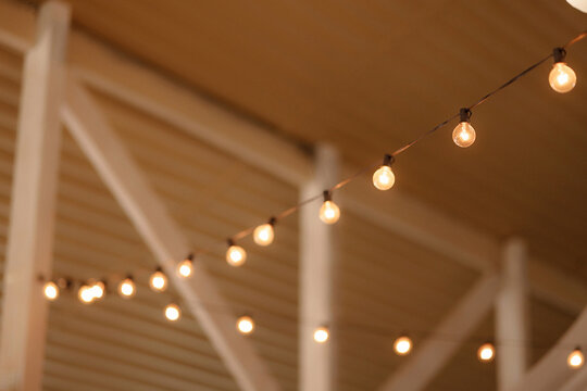 Glowing string lights hanging diagonally under a wooden ceiling in a cozy indoor space with copy space. Concept for decoration, celebration, festive mood, warm atmosphere.