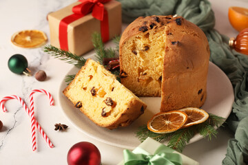 Plate with cut Panettone, dried orange slices, fir branches and Christmas decor on light background