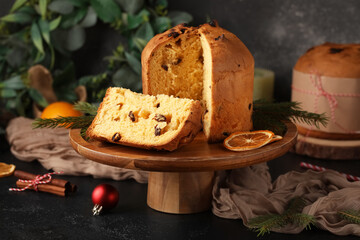 Wooden stand with cut Panettone, dried orange slices, fir branches and Christmas decor on black grunge background