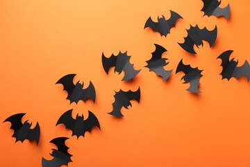 Halloween decor. Black paper bats on orange background, flat lay