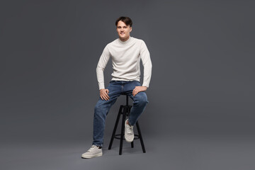 Man in stylish jeans on stool against grey background