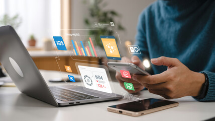 Person using smartphone with digital interface overlay next to laptop on a white surface indoors