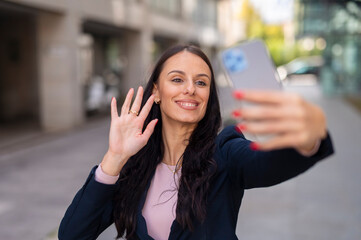 Businesswoman video calling and waving using smartphone outdoor