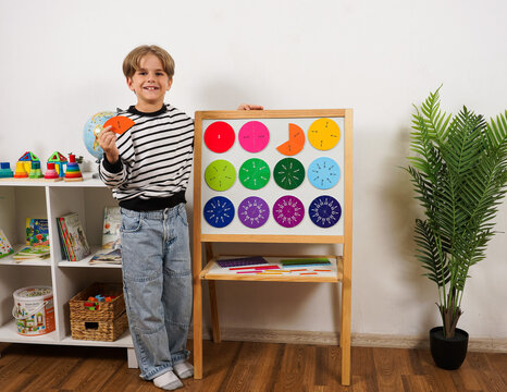 Happy schoolboy studying math fractions using colorful magnetic board in classroom. Concept of education, mathematics learning, STEM teaching, and visual study for elementary students.