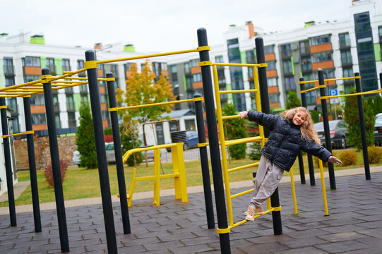 child playing on outdoor gym equipment in urban park. young girl enjoying healthy active lifestyle in modern playground setting amidst city buildings. vibrant autumn day outdoors