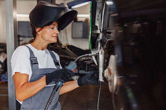A skilled female welder focuses on vehicle repair in a professional workshop to ensure quality work