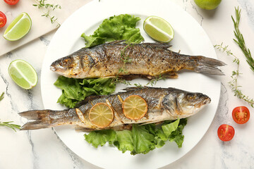 Plate with delicious cooked seabass fish, lettuce, herbs and lime slices on marble background