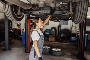 A highly skilled woman mechanic thoroughly inspecting the undercarriage of a car while in a modern garage setting