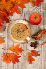 Indian masala chai with milk, ginger, anise, and cinnamon on an old wooden table with fallen autumn leaves. A traditional seasonal drink with spices, a cafe advertising card, a restaurant menu.