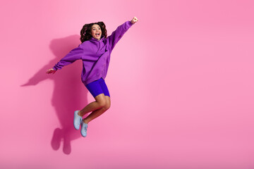 Energetic young woman jumping against pink background wearing vibrant sportswear and showing...
