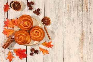 Cinnamon buns on wooden table with autumn fallen leaves, star anise, ginger and cinnamon, banner or display template, autumn greeting concept, menu mockup and advertisement for bakery.